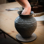 Eine Hand formt das Innere einer strukturierten, unfertigen Tonvase auf einem Holztisch mit "Feine Keramik von Hand formen - dein Einstieg in die Aufbautechnik" während des Töpferprozesses.