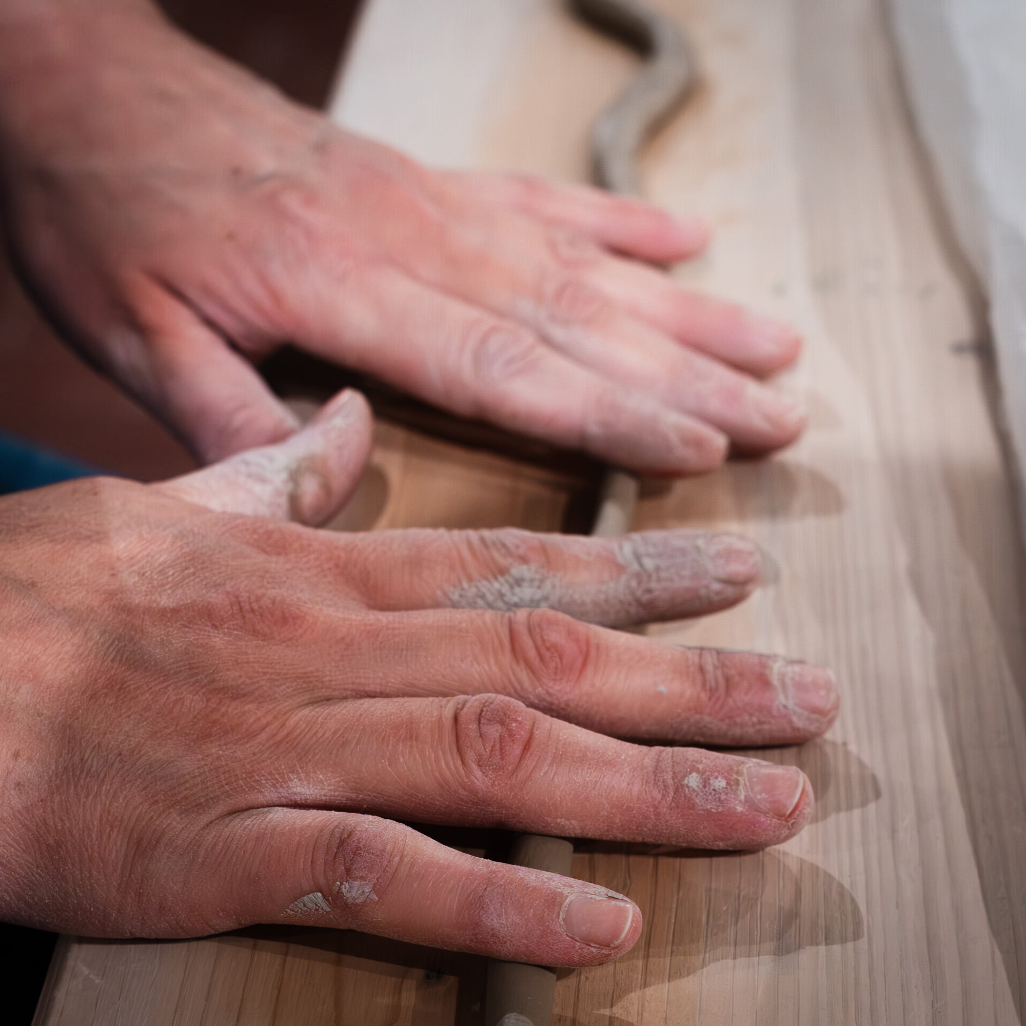Nahaufnahme der Hände, die ein dünnes Tonstück auf Holz formen, die Finger sind mit weißem Ton bestäubt, während sie "Feine Keramik von Hand formen - dein Einstieg in die Aufbautechnik" verwenden.