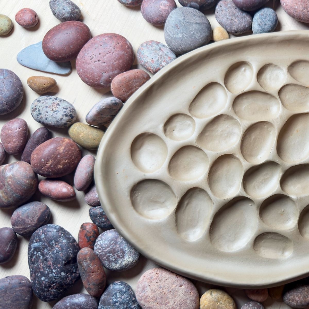 Das mit Plattentechnik gefertigte beigefarbene Tontablett mit ovalen Vertiefungen, die von Flusssteinen inspiriert sind, eignet sich perfekt für das kreative Schüsseln gestalten in der Keramikwerkstatt "Ton - Stein - Baum: Gestalten mit der Natur".