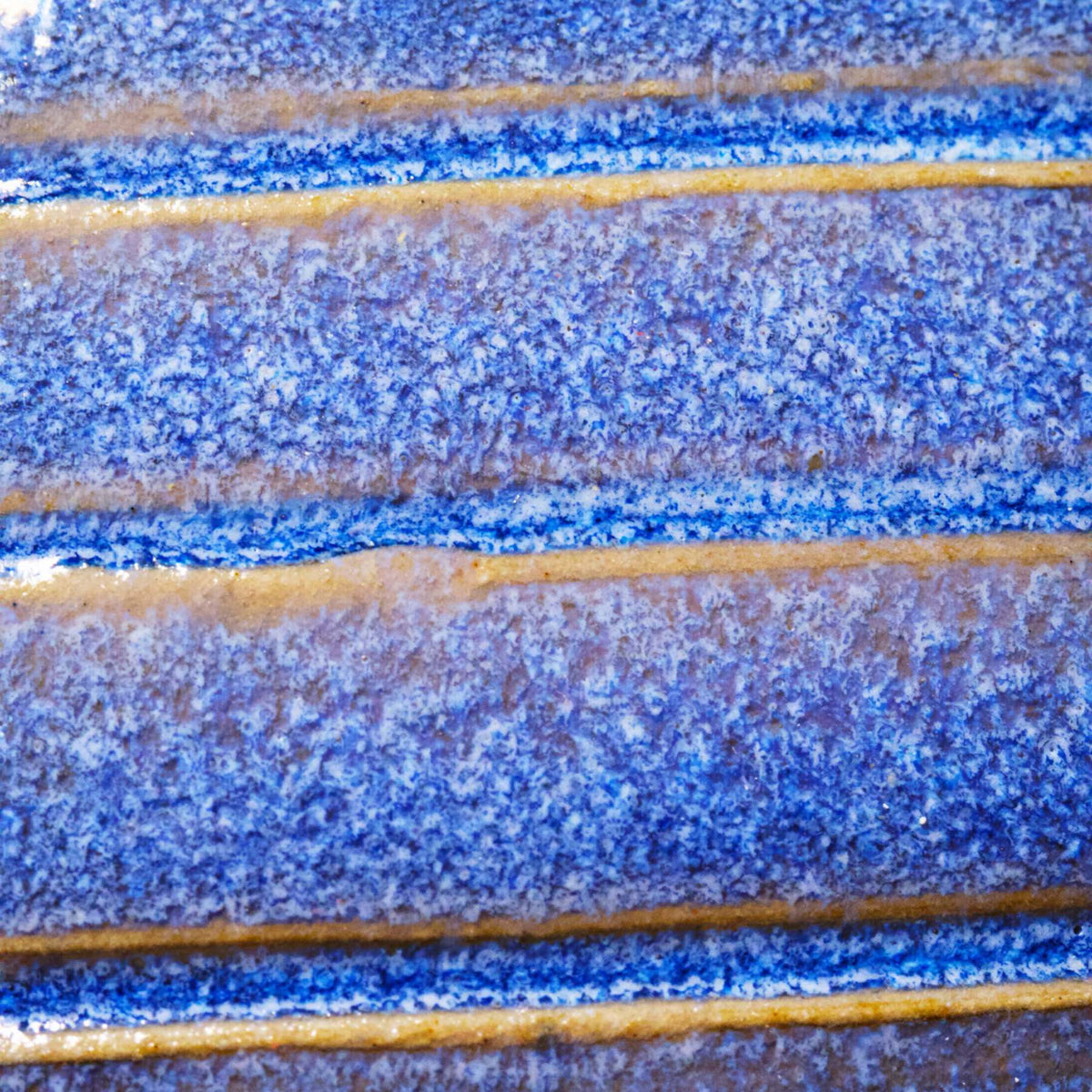 Nahaufnahme einer strukturierten blauen und gelben Glasur mit horizontalen Rillen - eine ideale Inspiration für Keramiker oder alle, die an der Masterclass teilnehmen: Glasuren entschlüsselt, um ihre eigenen einzigartigen Keramikoberflächen zu entwickeln.