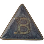 Botz Steinzeug: Ein glänzendes, dunkelblaugrünes Keramikdreieck mit einem erhabenen Buchstaben B in der Mitte. Bei 1220–1280 °C mit Steinzeugglasur gebrannt, zeugen seine leicht abgerundeten Kanten und die strukturierte, reflektierende Oberfläche von hochwertiger Handwerkskunst.