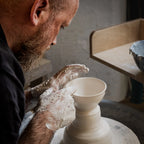 Ein bärtiger Mann formt in einem Atelier einen Tontopf auf einer Drehscheibe, seine Hände sind mit nassem Ton bedeckt, während er sich konzentriert - ein Beispiel aus der "Masterclass": Serien drehen.