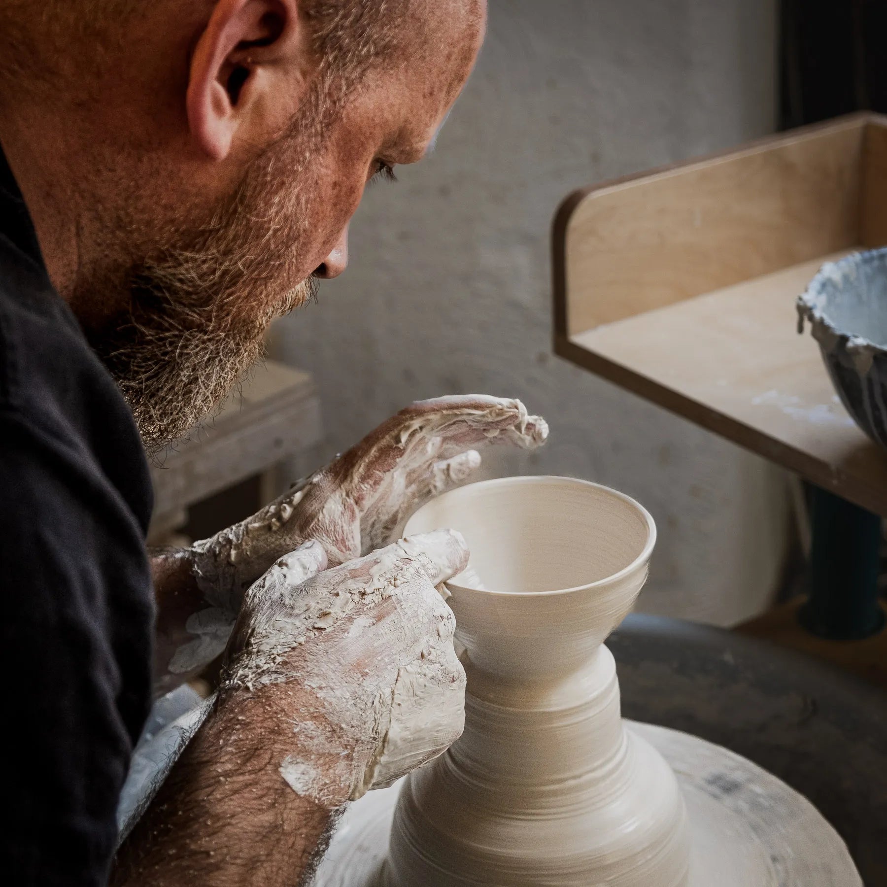 Ein bärtiger Mann formt in einem Atelier einen Tontopf auf einer Drehscheibe, seine Hände sind mit nassem Ton bedeckt, während er sich konzentriert - ein Beispiel aus der "Masterclass": Serien drehen.