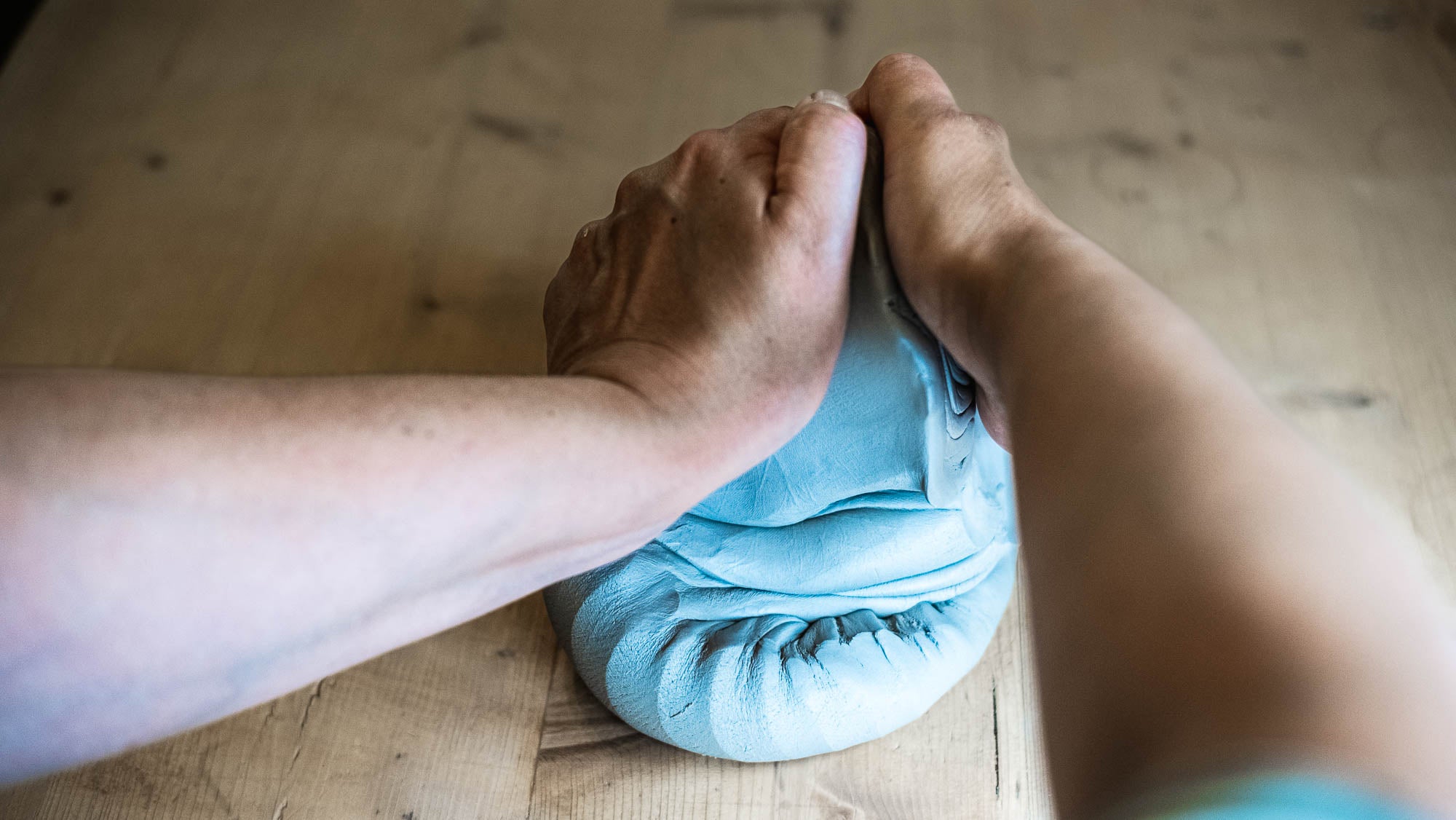 Eine Person knetet hellblauen Teig auf einer Holzoberfläche und faltet und formt ihn mit beiden Händen.