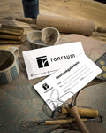 Ein Geschenkgutschein liegt auf einem Tisch mit Töpferwerkzeug, Rollen, einer Keramiktasse und Tonstücken mit Blumenmustern – ideal, um Töpferkurse zu verschenken und Kreativität zu fördern.
